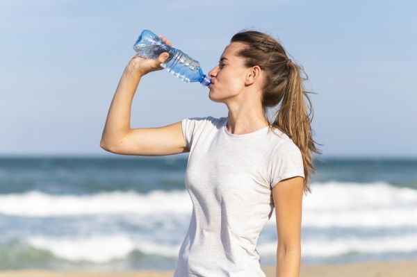 ung kvinna dricker vatten pa sandstrand